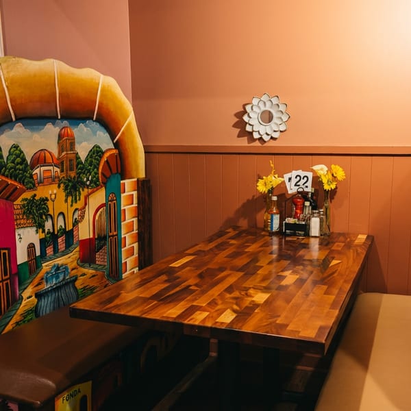 A vibrant Mexican restaurant booth with a wooden table, colorful painted backrests, and sunflowers.