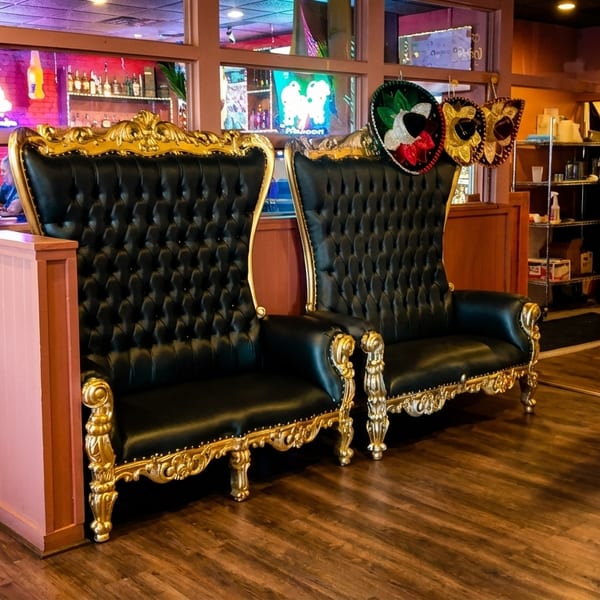 Two ornate black and gold chairs with sombreros, a colorful bench, and restaurant patrons.