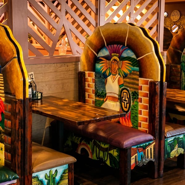 Restaurant interior with three booths featuring vibrant, hand-painted Mexican-themed murals on the chair backs.
